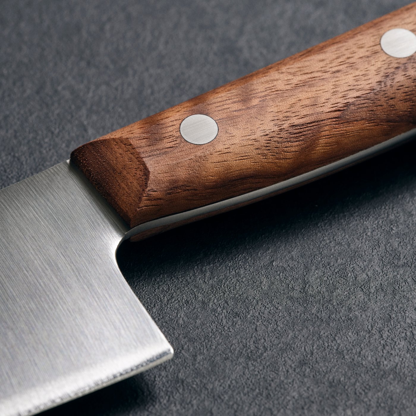 Couteau de cuisine VARDAGEN posé sur une surface sombre. Il est doté d’une lame en acier inoxydable et d’un manche en bois avec rivets métalliques.
