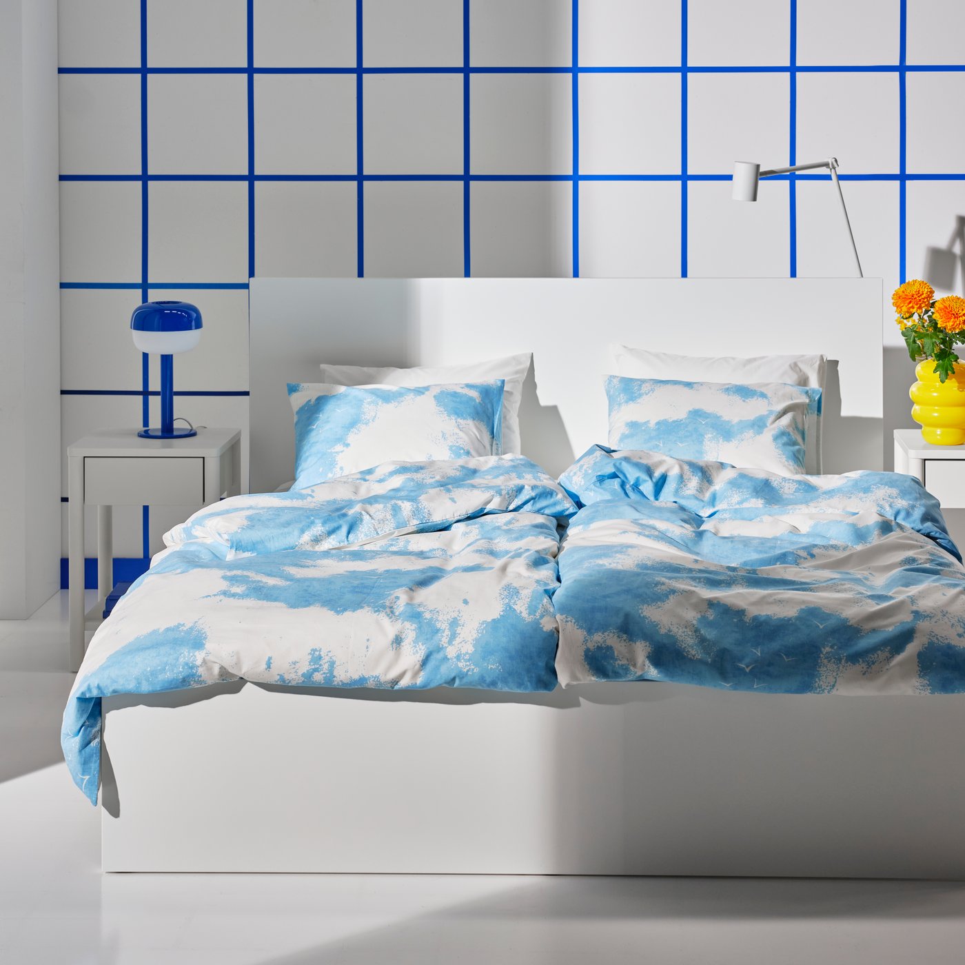 A white double bed made with ÄNGSVITVINGE duvet covers and pillowcases with a blue and white pattern.
