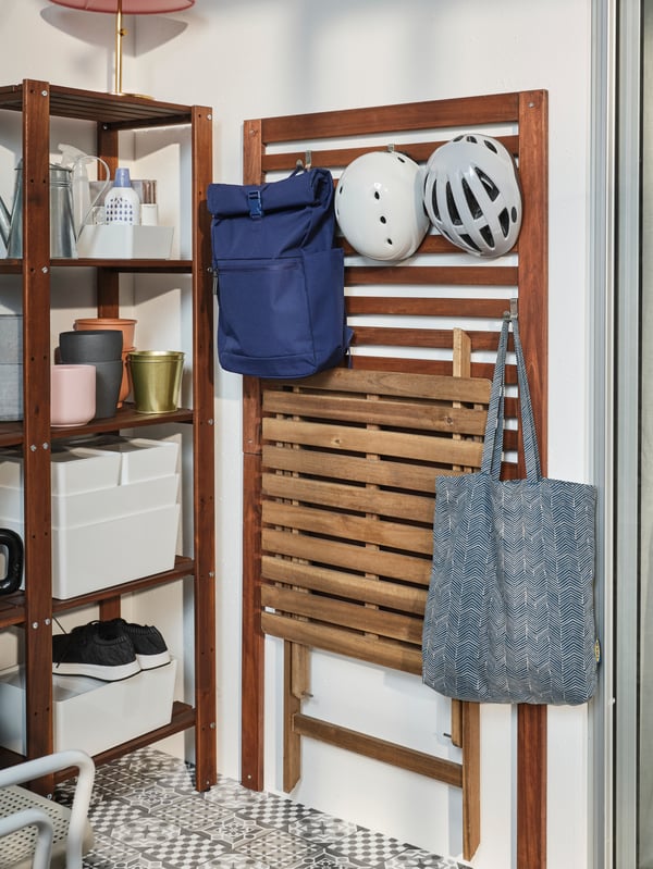 A brown-stained wall panel with hooks mounted to a wall. Two bags, a folded table and two helmets hang from the hooks.