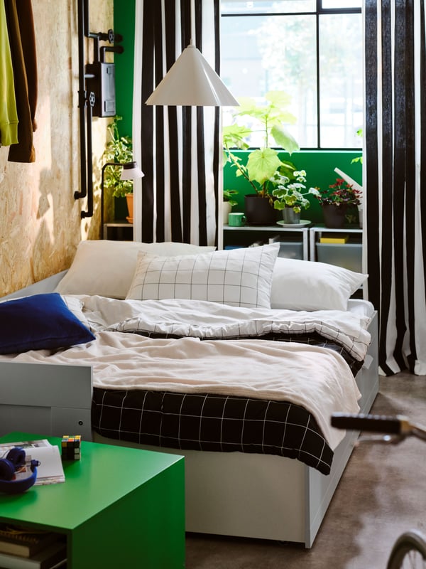 A grey BRIMNES day-bed with 2 drawers opened as a double bed, with a white/black check VITKLÖVER comforter set on top.