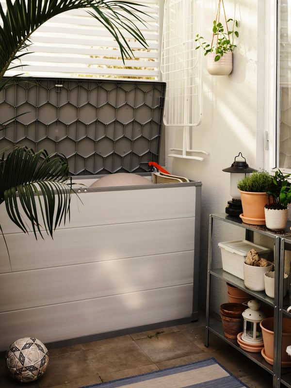 Une boîte de rangement VRENEN gris clair, couvercle ouvert, un séchoir MULIG blanc accroché au mur, des étagères avec des plantes.