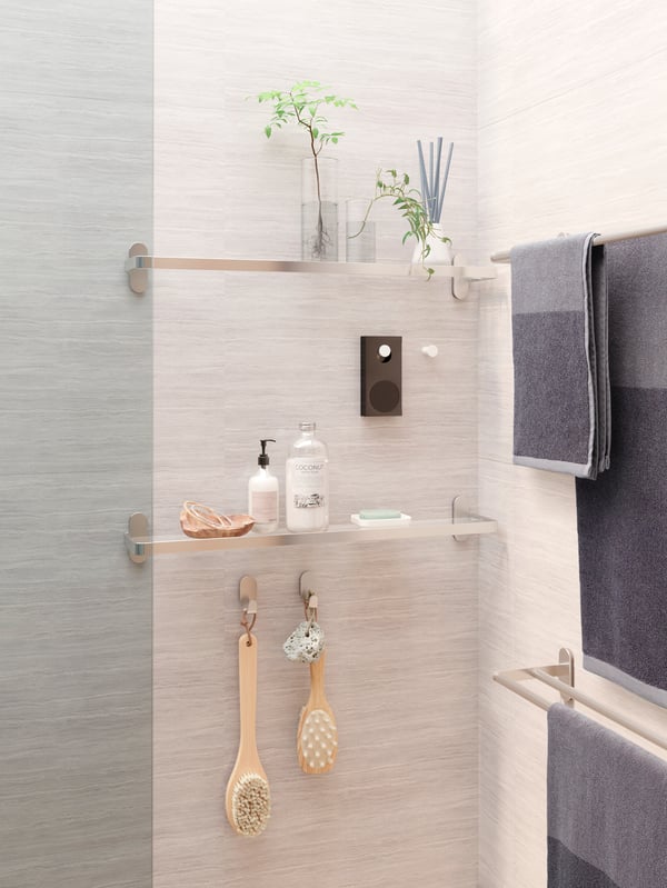 A grey shower with glass shelves with decorative items and shower products, an ENEBY speaker hanging from a white knob.