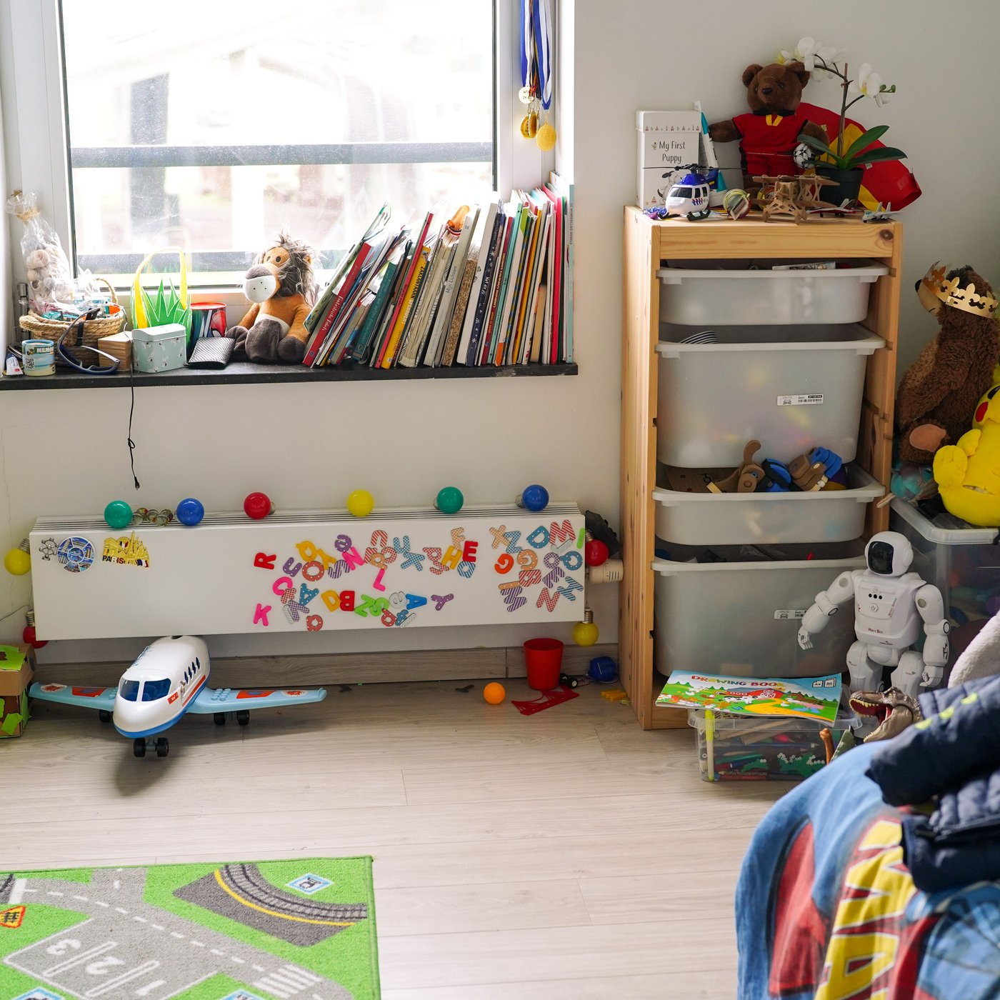 Svetla dečja soba s IKEA TROFAST rešenjem za odlaganje ispunjenim igračkama i knjigama na prozoru.