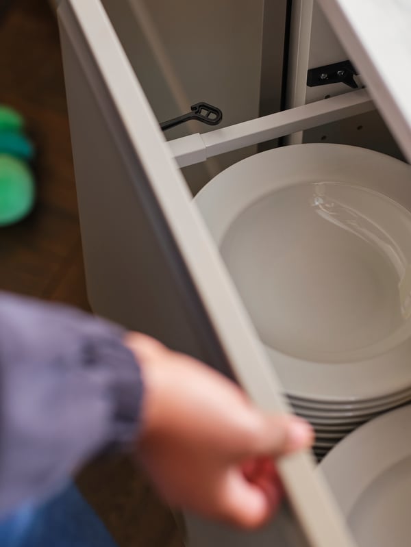 Ruka koja otvara kuhinjsku fioku s crnom UTRUSTA bravom za kuhinjske fioke/elemente u kojoj su beli duboki tanjiri.