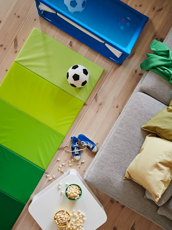 A black-and-white SPARKA toy football on a green PLUFSIG gym mat placed in front of a blue SPORTSLIG toy goal with storage.