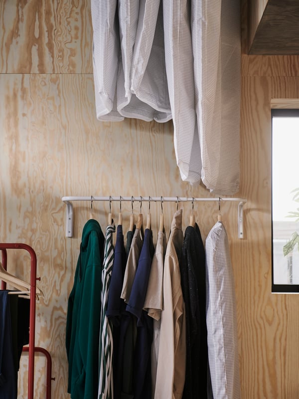 A white chest of drawers with boxes on top. A clothes bar hangs above it with shirts and jeans on hangers.