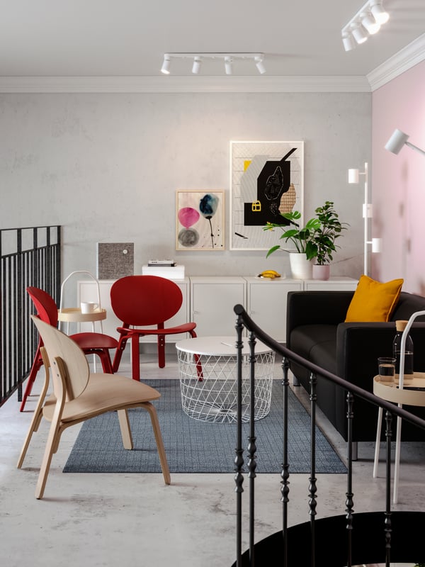 A lounge area with a black sofa, red easy chairs, colourful art on the wall, a white storage table.