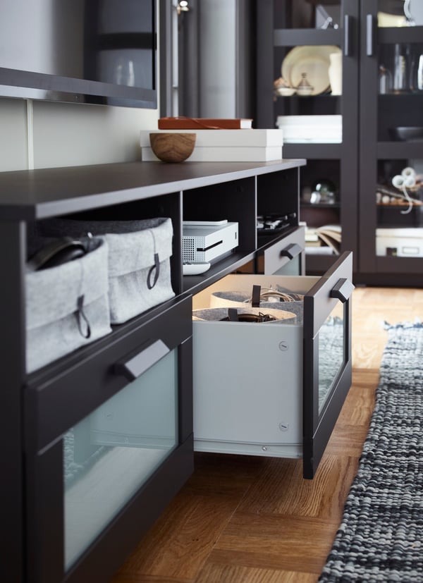 A black BRIMNES tv bench sits underneath a big TV. One drawer is pulled out containing inserts. Felt boxes line the shelves.