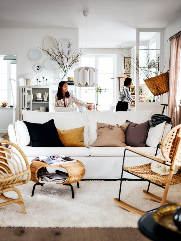 A white BACKSÄLEN sofa and two armchairs in a bright country-style living area with two women at the back of the room.