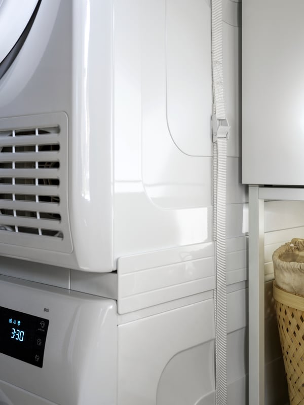 An IKEA 500 UDDARP tumble dryer on top of a washing machine, supported by the TYKARP shelf in between.