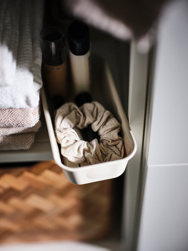 A white plastic NOJIG organiser holding a hair scrunchie and toiletries on a shelf.