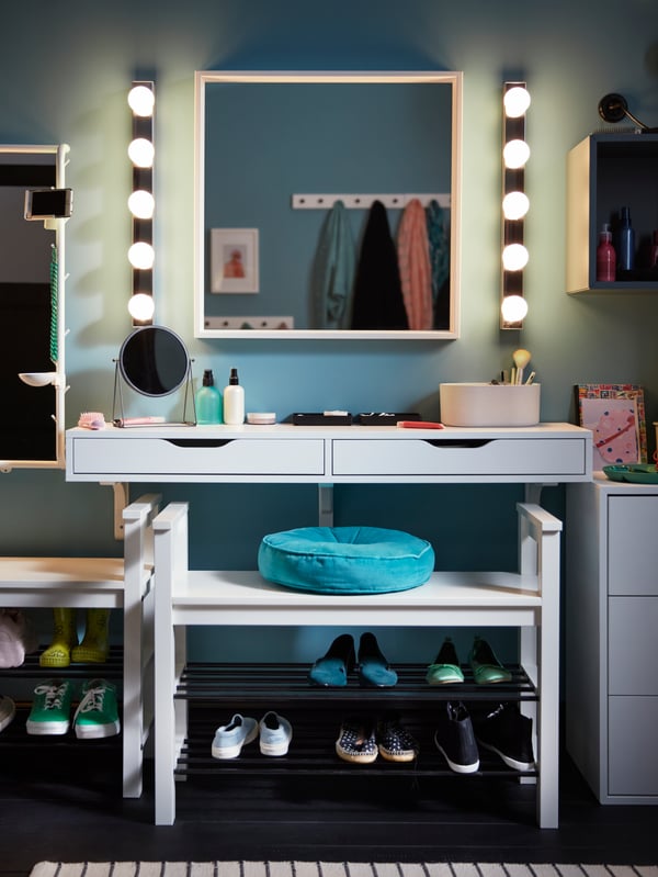 A white EKBY ALEX wall shelf with drawers and makeup products on top, plus a white mirror with wall lights on each side.
