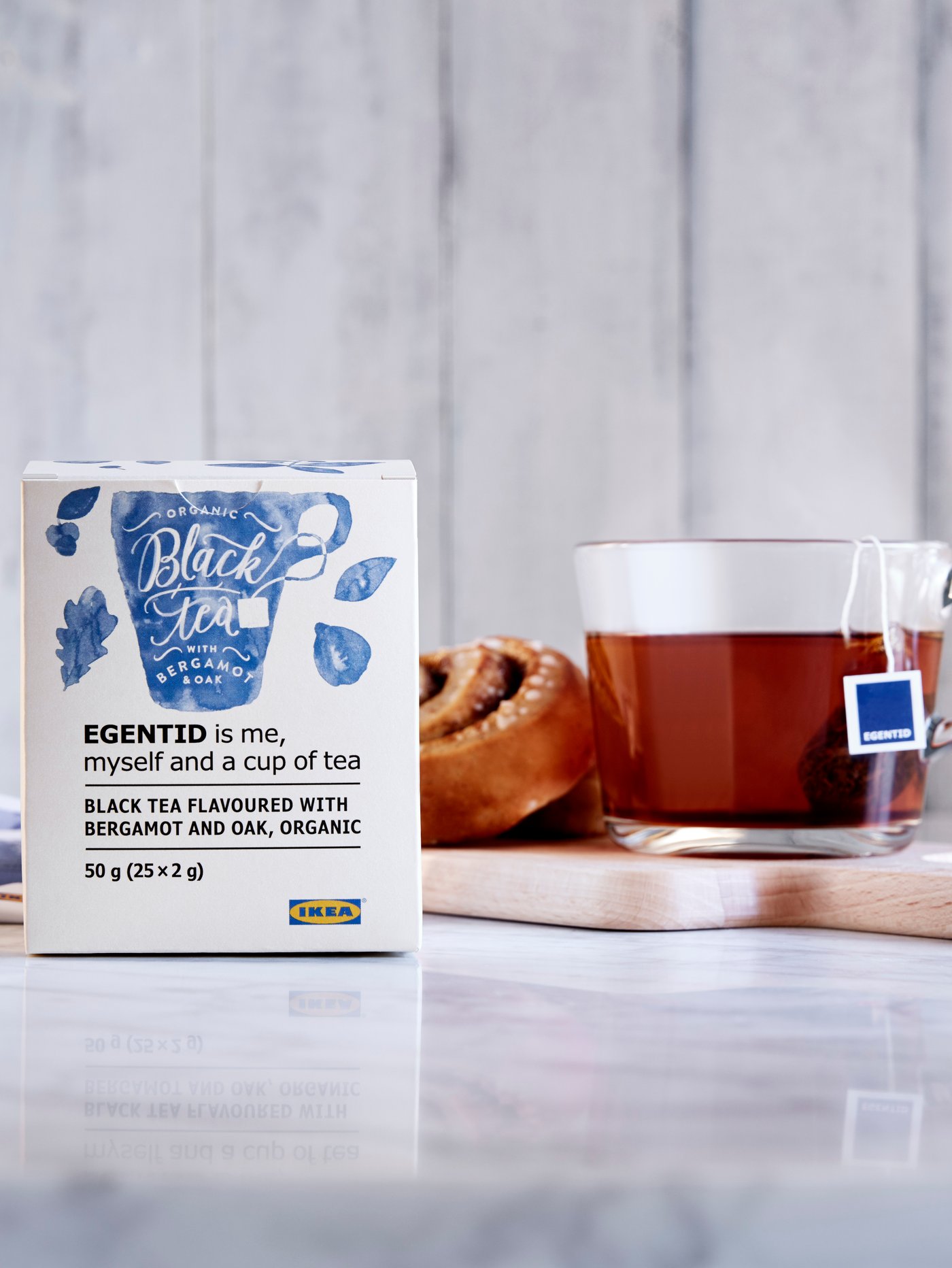 Zimtschnecke neben einer Tasse Tee in einem Glasbecher auf einem kleinen Tablett; davor steht eine Packung EGENTID Tee.