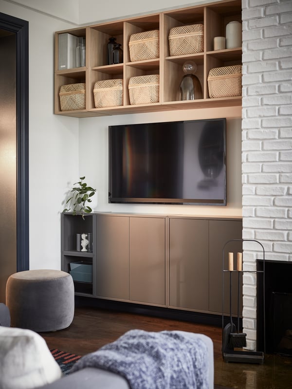 A wooden open storage cabinet above the TV with bamboo baskets and vases, and a dark gray cabinet with doors below the TV.