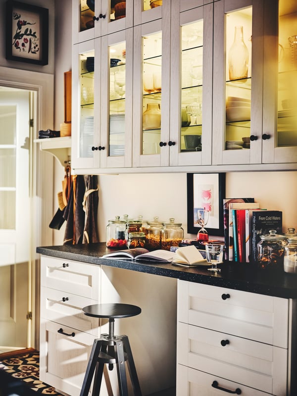 A kitchen with white ENKÖPING drawer fronts, wall cabinets with white ENKÖPING glass doors and a DALFRED bar stool.