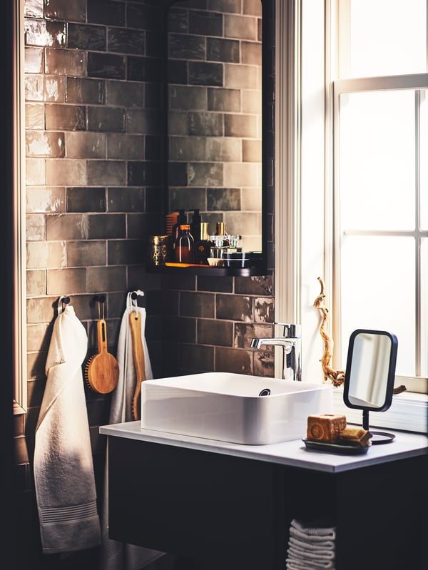 A bathroom with a dark grey GODMORGON wash-stand, a black LINDBYN table mirror and accessories hung from SKOGSVIKEN hooks.
