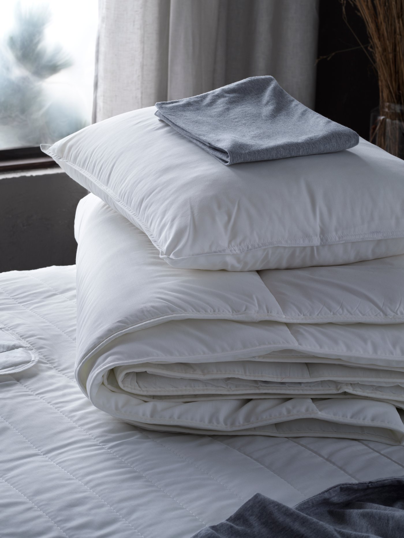 SMÅSPORRE duvet and pillow in a stack on top of a mattress next to the window in a bedroom setting.