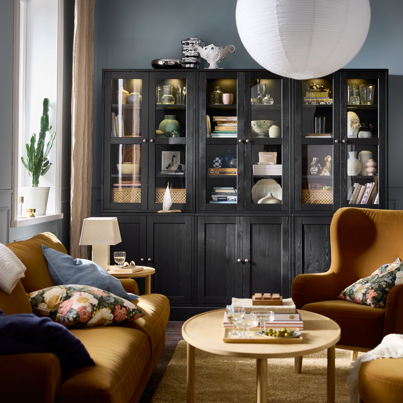 A living room featuring a black HAVSTA storage combination with glass doors, arranged with decorative items and plants.
