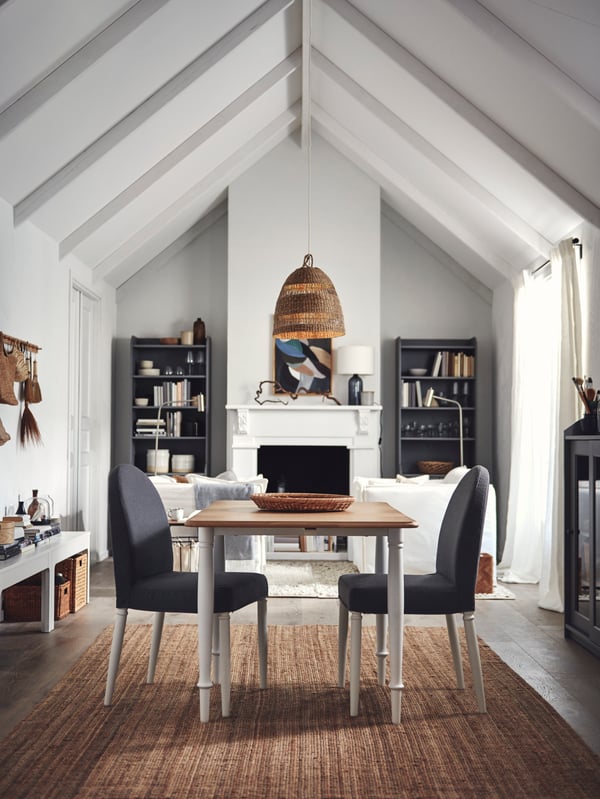 A white-and-oak-veneer DANDERYD drop leaf table with two DANDERYD chairs stand in the middle of a light spacious living room.