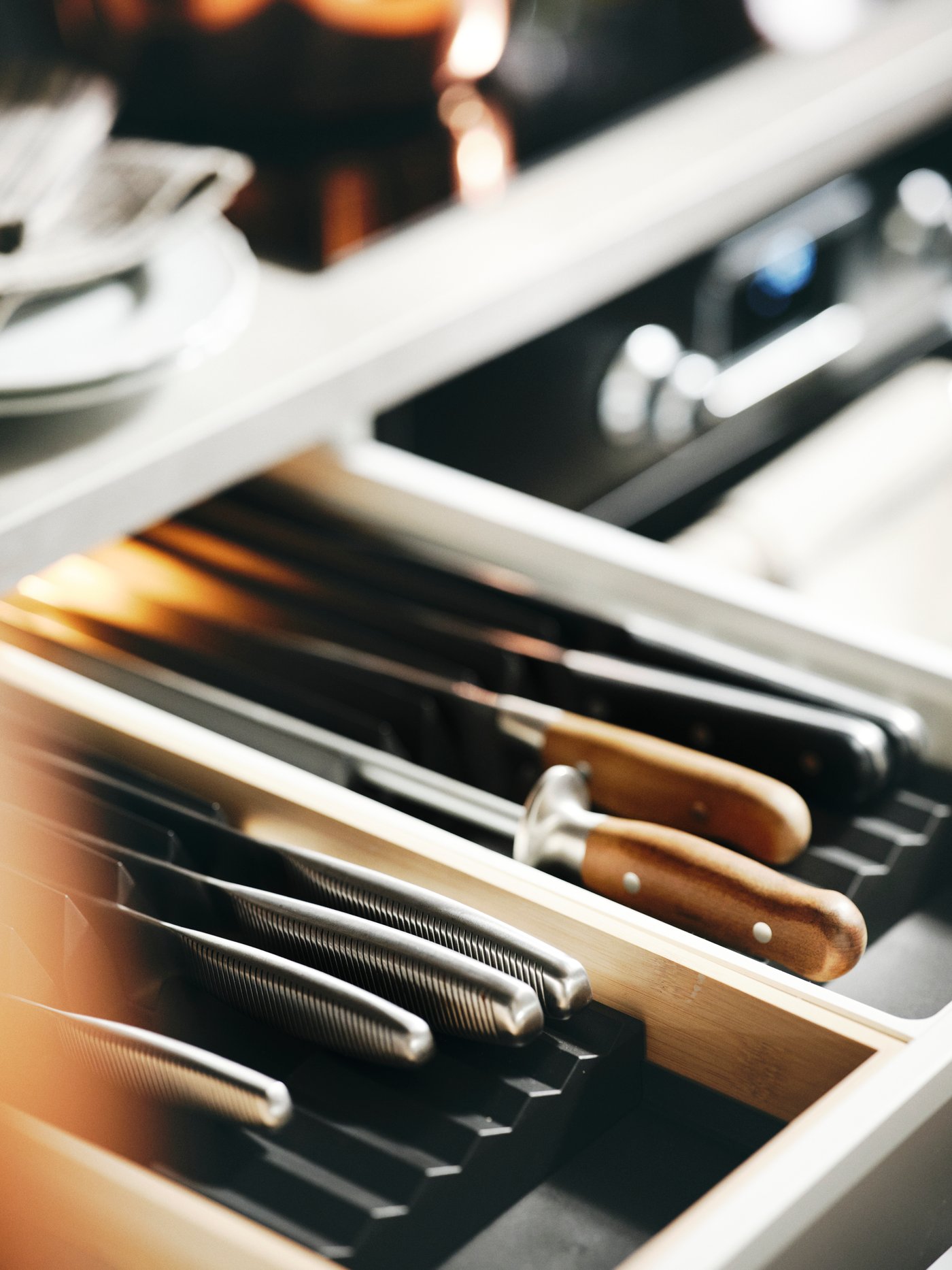 An open kitchen drawer revealing two anthracite UPPDATERA knife racks holding kitchen knives and a BRILJERA knife sharpener.