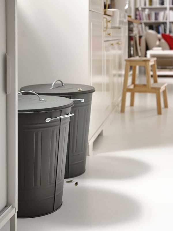 Two grey KNODD bins with lids in a white kitchen, plus an aspen step stool, a sofa and two white bookcases.
