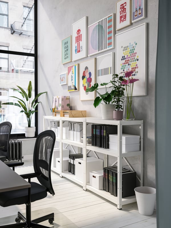 White shelving units with black folders and white boxes, colourful framed art on the wall, black office chairs.