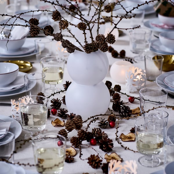 A white-themed dinner table is decorated for Christmas with a VINTERFINT vase.
