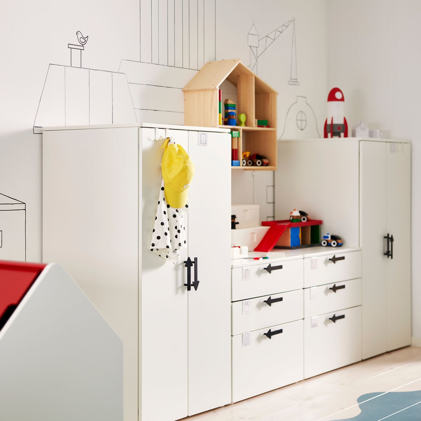 White SMÅSTAD/PLATSA storage units with JÄRNSPARV black handles against a wall with a FLISAT doll’s house/shelf on it.