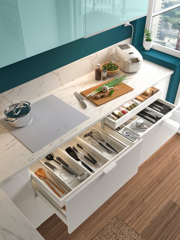 A kitchen setting featuring opened METOD drawers with UPPDATERA cutlery trays inside.