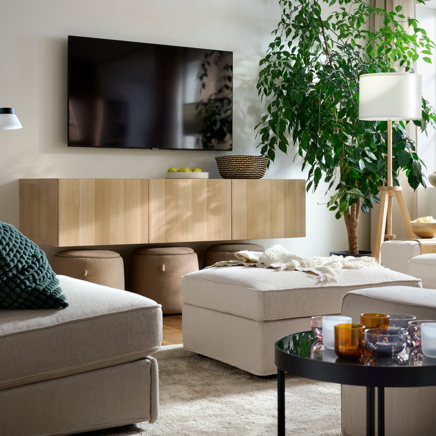 A light, bright living room with a combination of KIVIK seating, a STOENSE rug, a wall-hung TV and a big, leafy plant.