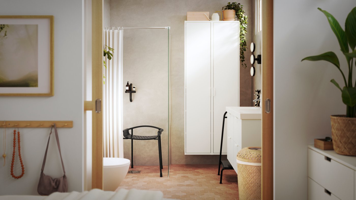 A bright bathroom is seen from a bedroom, and it has white HAVBÄCK bathroom furniture and BÄSINGEN accessories in anthracite.