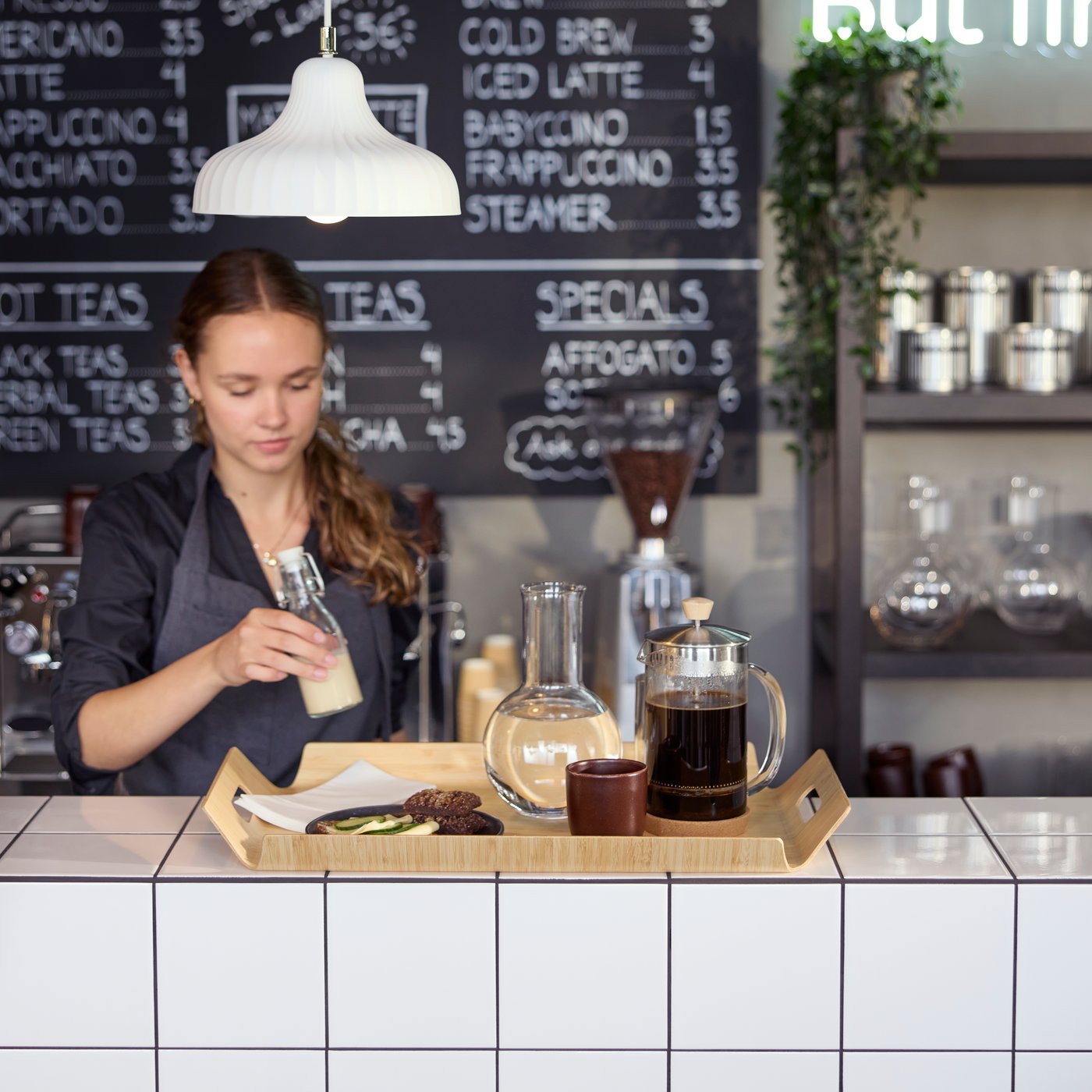 Café scene with a barista preparing  a bamboo SILVERHAJMAL tray to serve drinks and food on a tiled café counter.