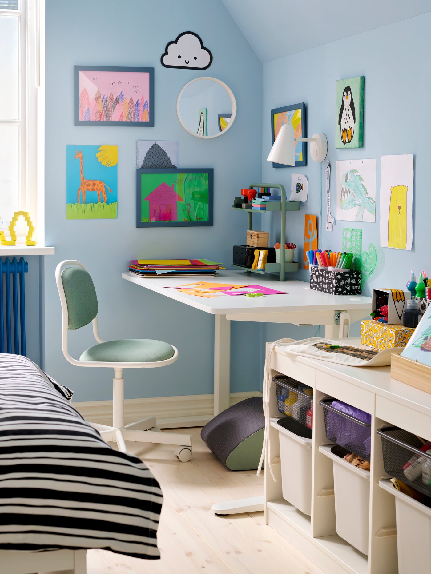 The corner of a children’s room with light blue walls, RELATERA desk and lots of colourful drawings on the walls.