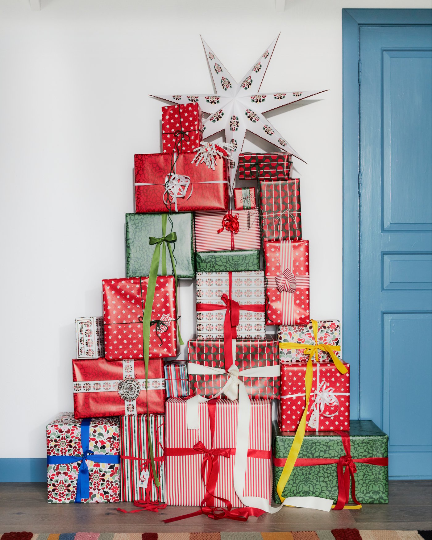 A Christmas tree made of Christmas packages stands in the room. On the top package is added STRÅLA lampshade. Everything looks like a Christmas tree.