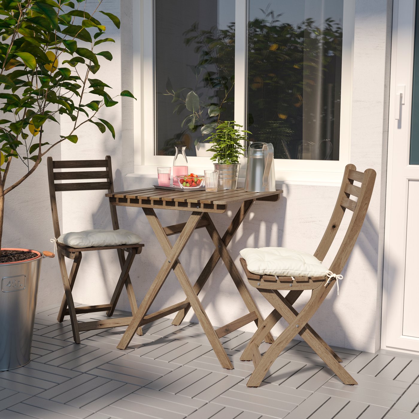 Juego de terraza ASKHOLMEN pequeño con dos sillas y una mesa pegada a la pared. Hay plantas en ambos lados y encima de la mesa.