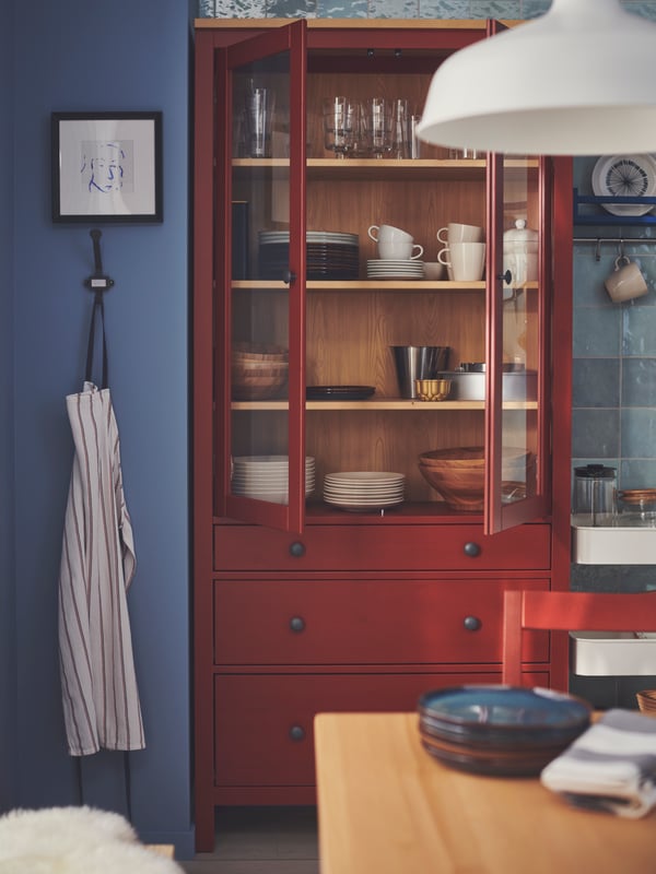 HEMNES vitrina s 3 fioke u kojoj je razno stono posuđe nalazi se pored plavog zida, u blizini stola na preklop.