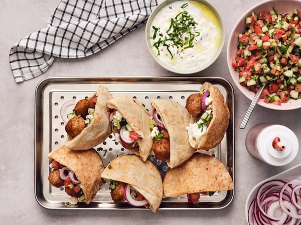 Meatballs & tzatziki in Greek pita bread on a baking tray with red onion.