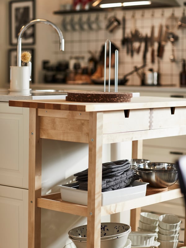 Una cocina luminosa cuenta con un carrito de cocina FÖRHÖJA con diversos utensilios de cocina almacenados en los estantes y en la encimera.
