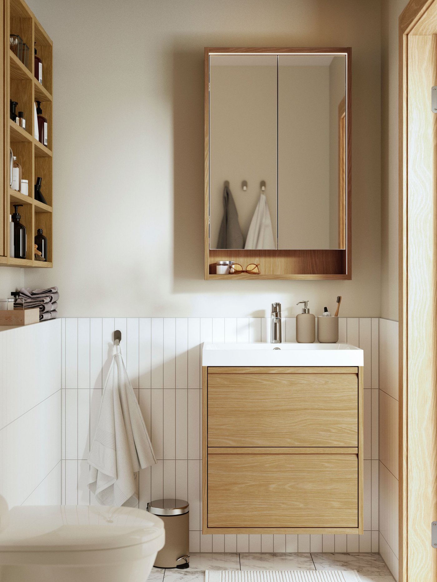 Ein helles Badezimmer mit Holzwaschtisch und Spiegelschrank wirkt schlicht und modern. Handtücher, Pflegeprodukte und offene Regale sorgen für eine aufgeräumte, warme Atmosphäre.