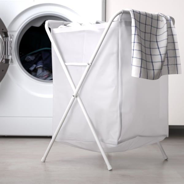 Sac à linge en plastique avec support en métal pliant JÄLL blanc rempli de vêtements, devant un lave-linge.