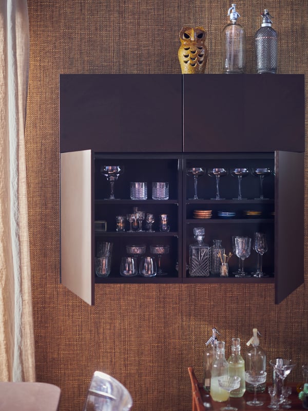 A BESTÅ wall cabinet with HEDEVIKEN doors. Two doors are open, showing glasses, coasters and cocktail-making accessories.