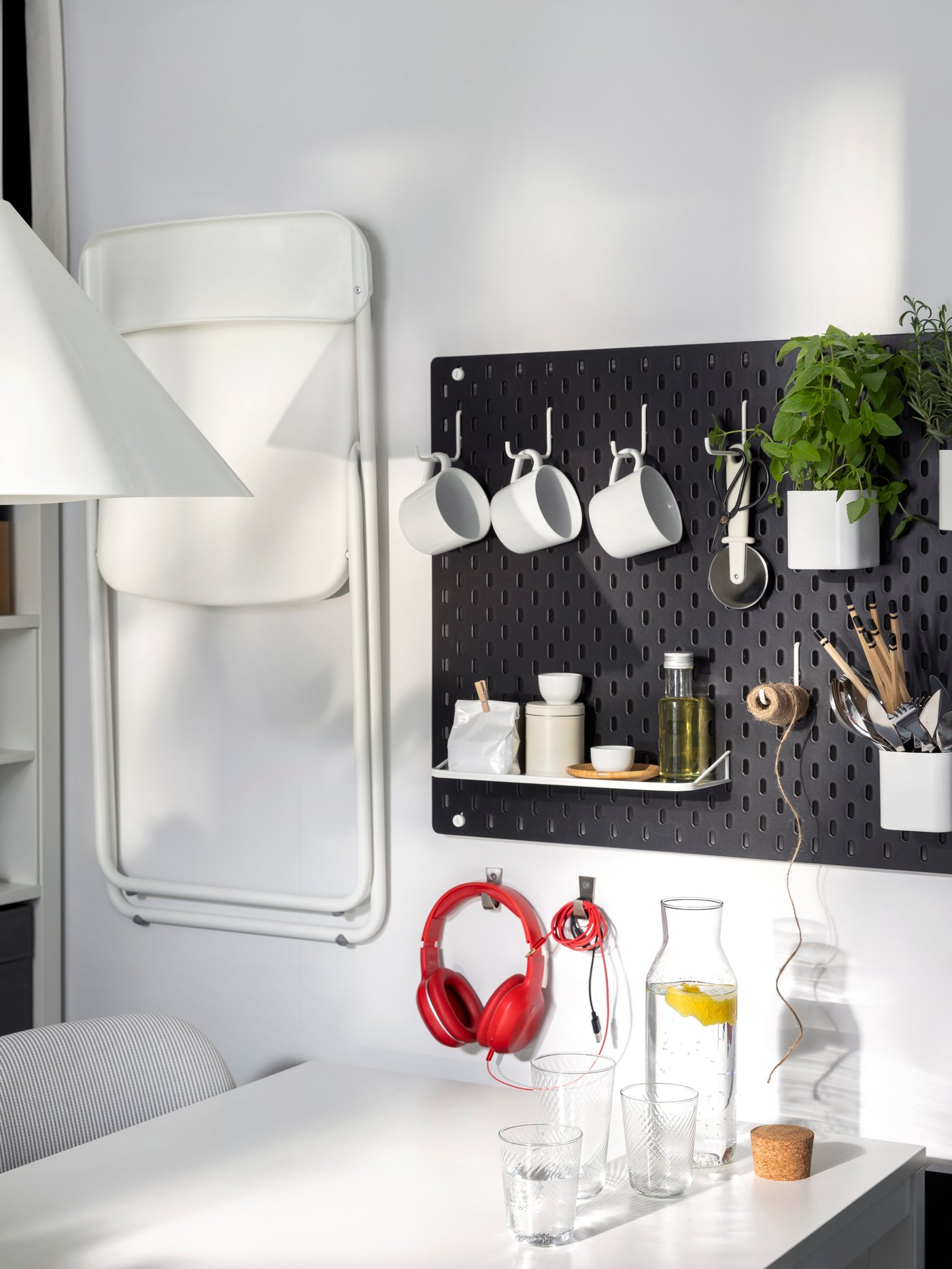 Twee SKÅDIS ophangborden en een VIHALS klapstoel hangen aan de muur naast een witte VIHALS uittrekbare tafel.