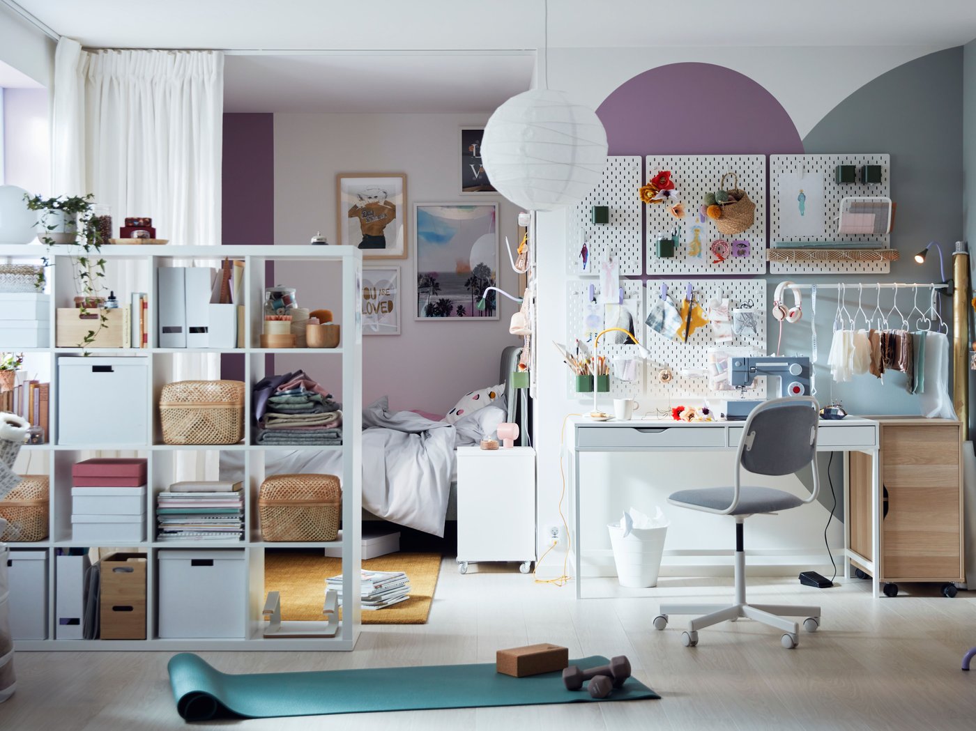 A bright, colourful room with pegboards over an ALEX desk, and curtains and a KALLAX shelving unit sectioning off a bed.