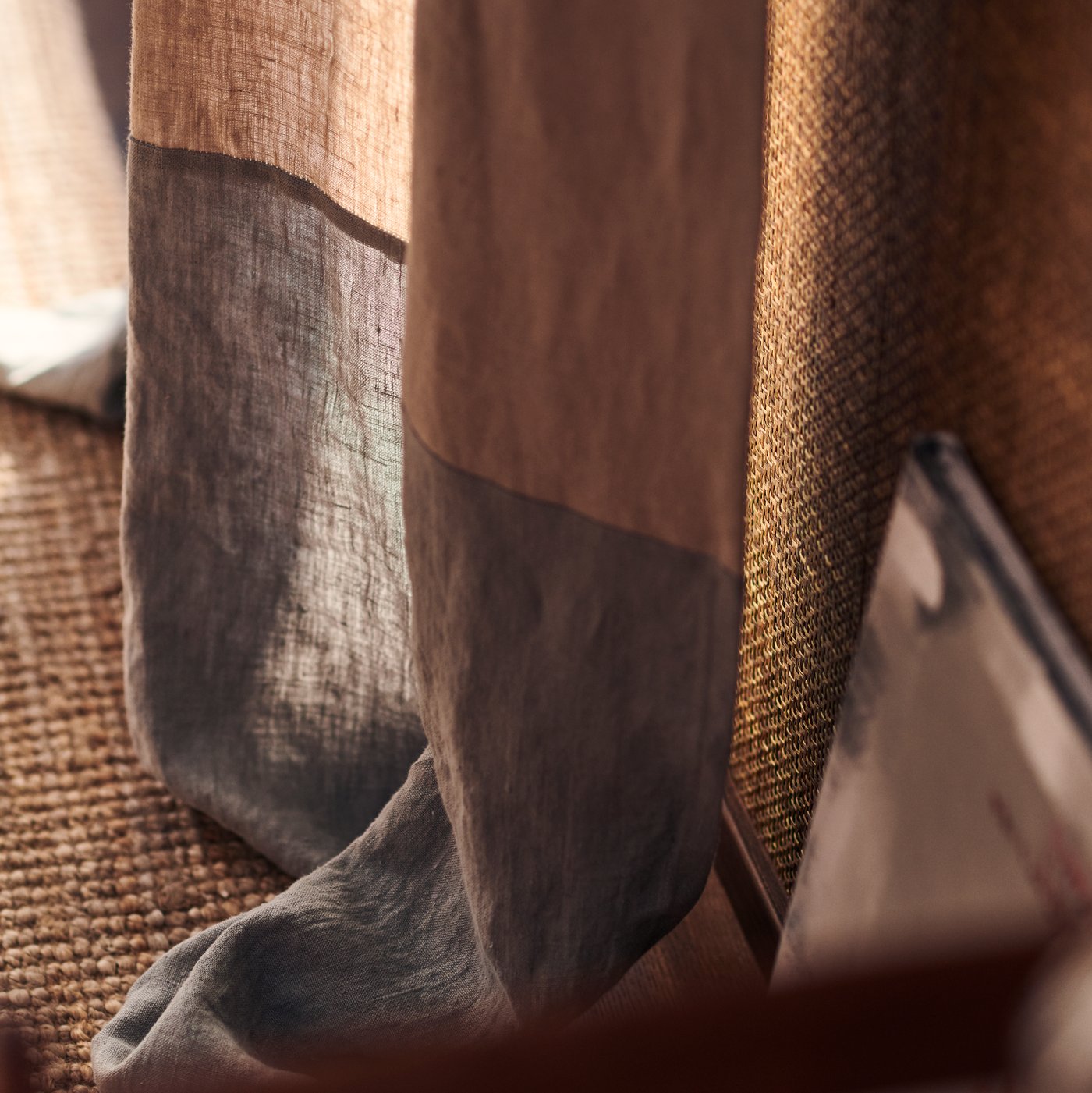 The bottom part of a brown and grey colored curtain, falling onto a LOHALS rug in jute.