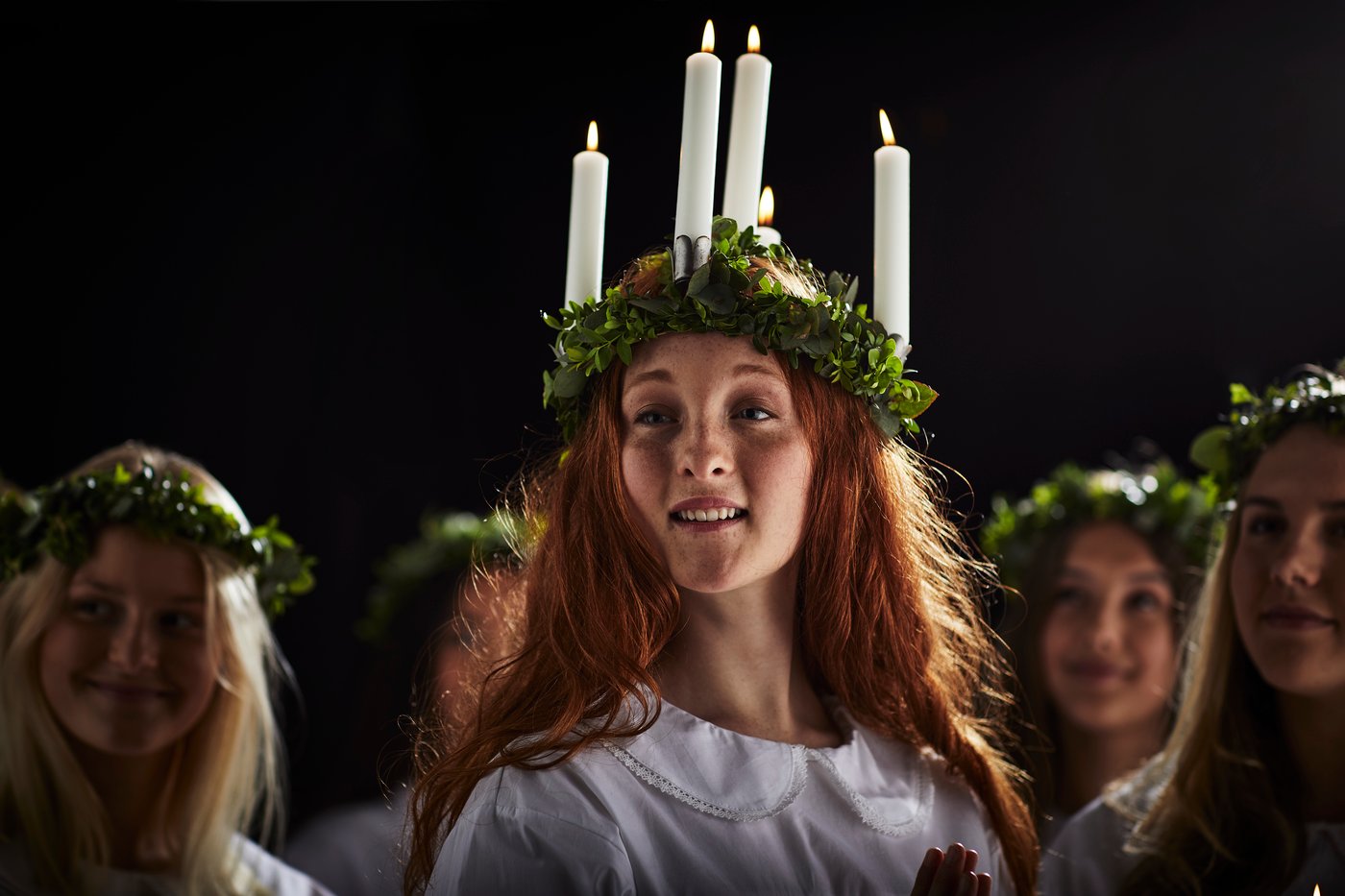 A woman with red hair wearing a crown made of leaves and candlesticks for Santa Lucia celebrations.