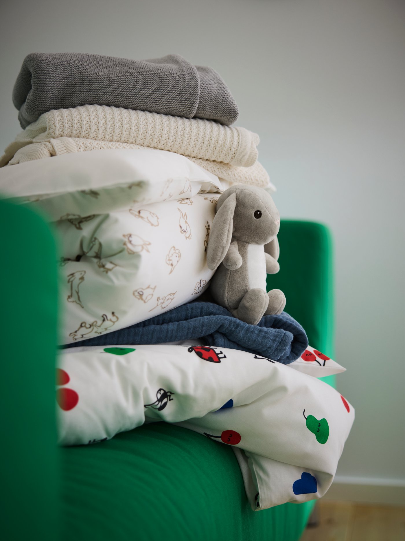 A pile of bedding for a cot: duvets, pillows, blankets and throws. Next to it sits a DVÄRGHARE soft toy.
