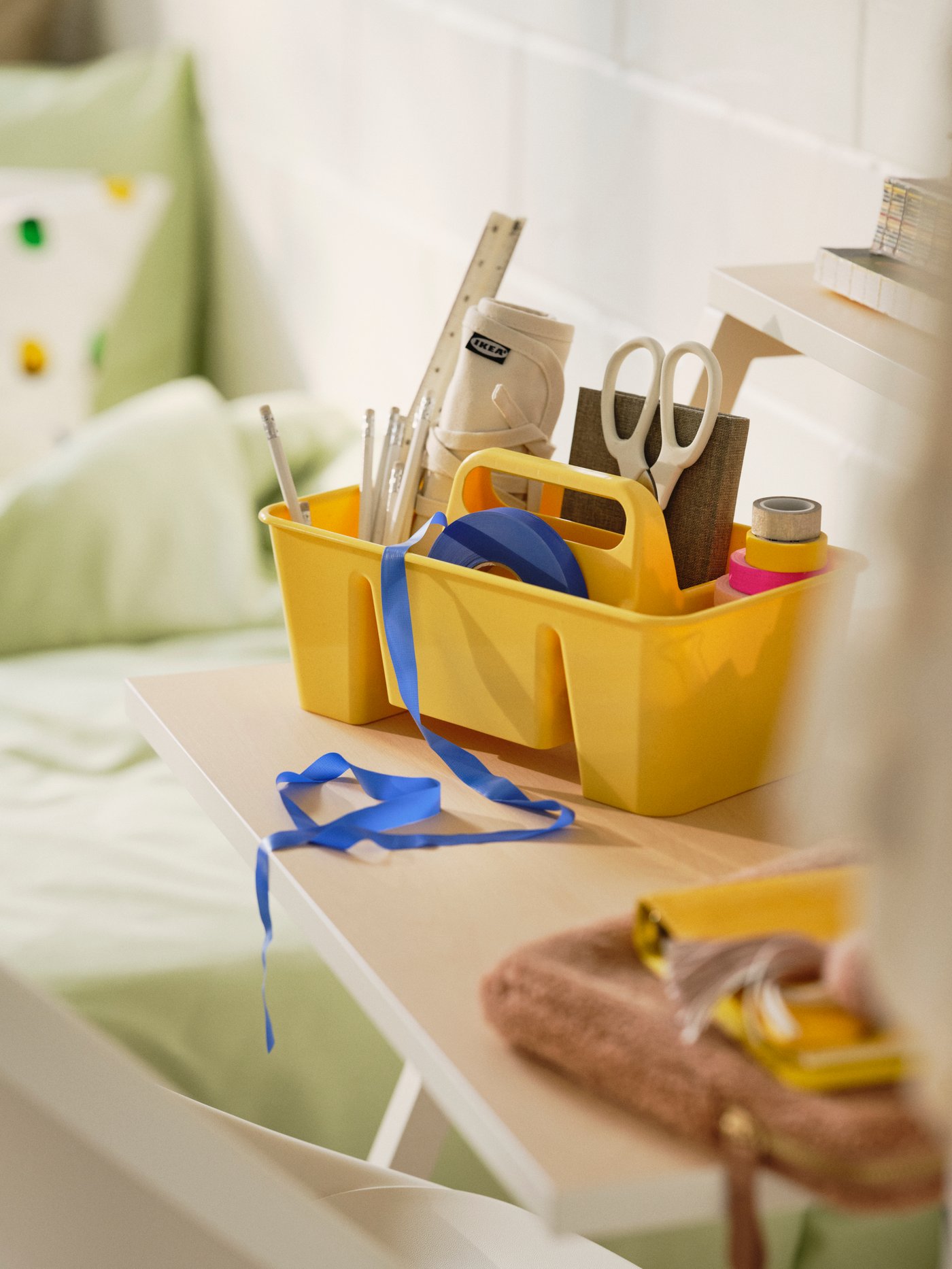 Close-up of small yellow portable storage with handles filled with stationary on white student desk in college dorm room.
