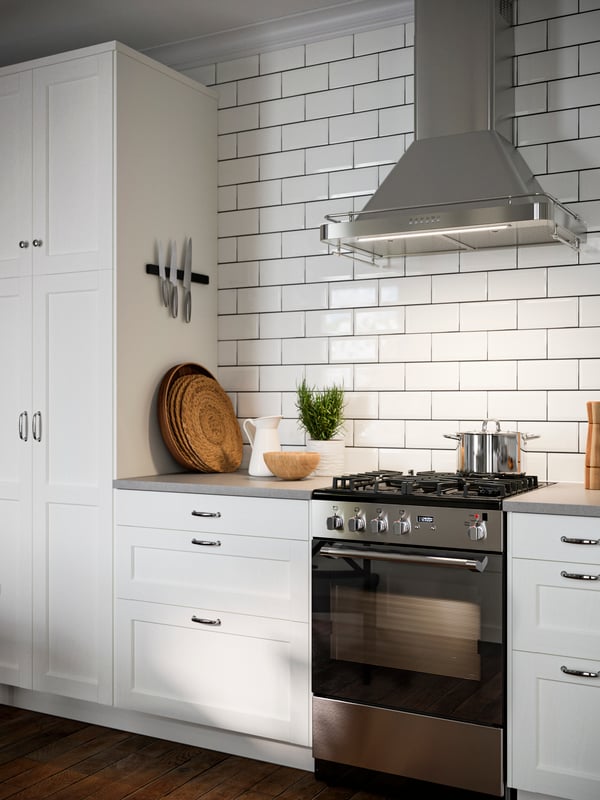 Una cocina con frentes ENKÖPING blancos, campana extractora de pared ALLMÄNBILDAD en acero inoxidable, elementos en la cubierta.