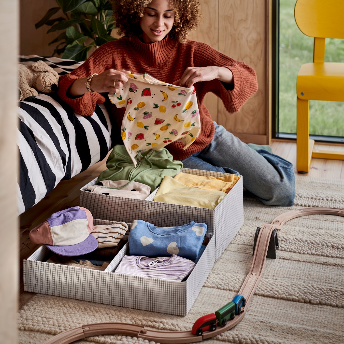 A person sits on the floor and organises clothes into two different sized STUK boxes with compartments.
