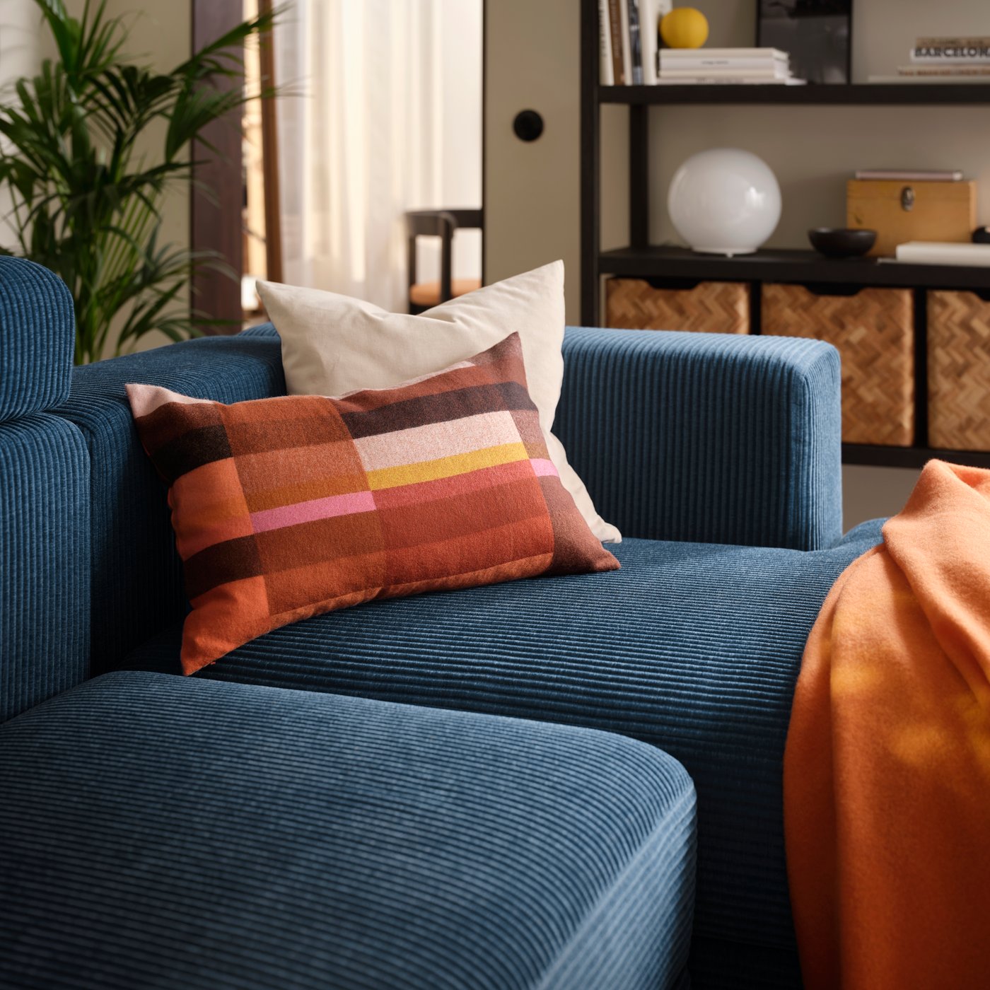 A living room with a dark-blue JÄTTEBO four-seat modular sofa with a chaise longue, holding a pair of cushions and a throw.